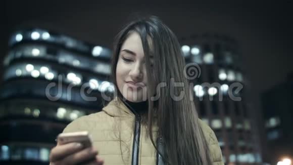 女人晚上在美丽的建筑背景下使用手机特写视频的预览图