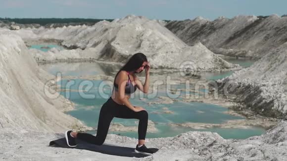 穿着黑色运动服的运动型黑发女孩在一个蓝水白垩沙场上训练每条腿上的午餐视频的预览图