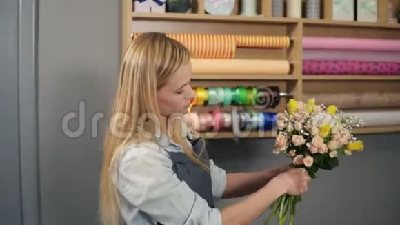 年轻的金发女花匠把一束黄色的郁金香和奶油玫瑰绑在手里手里拿着丝带视频的预览图