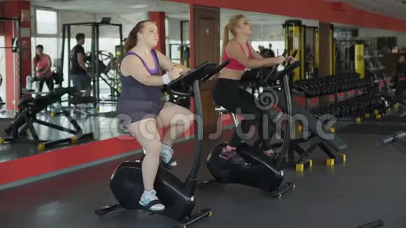 在健身房懒惰超重的女性在骑固定自行车时吃面包视频的预览图