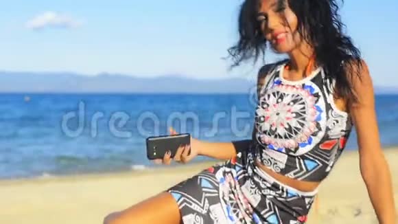 年轻的黑发女人在海滩上宣布打电话给她的手机视频的预览图