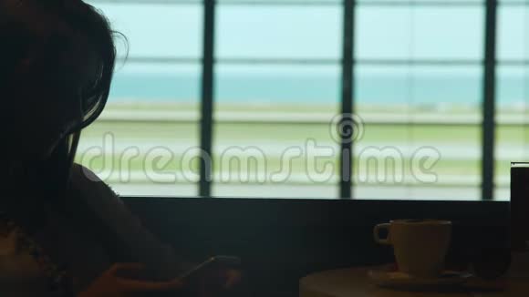 年轻微笑的女人在机场咖啡厅喝咖啡打手机视频的预览图