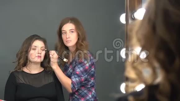 年轻女性客户照镜子的镜子而化妆师在她的眉毛上工作视频的预览图