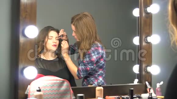 年轻的女客户照镜子而化妆师则在美容院工作视频的预览图