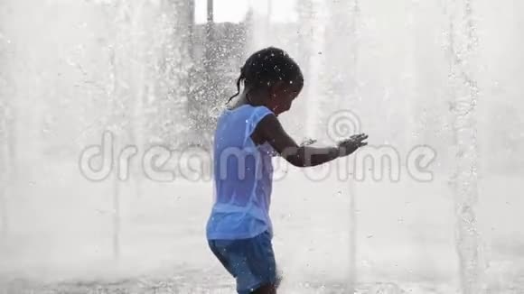 湿漉漉的小女孩在城市公共公园的喷气式喷泉里跑步和玩视频的预览图