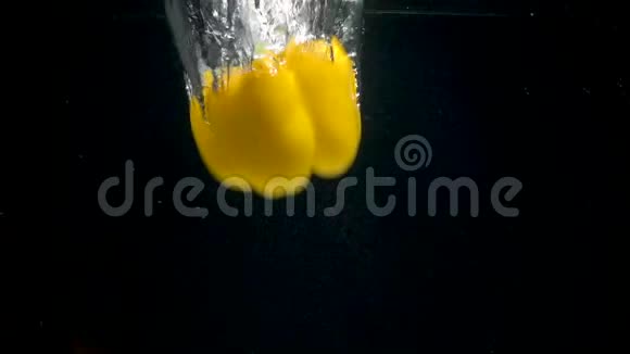黑色背景下黄色胡椒在水中落下的视频视频的预览图