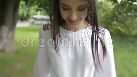 年轻迷人的女人带着美丽的微笑走在绿色公园里这位深色头发的人穿着刺绣连衣裙视频的预览图