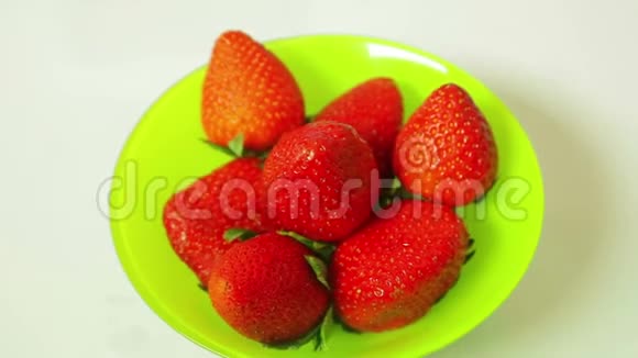 蓝色背景的绿色盘子里的红色新鲜草莓浆果在一个圆圈中旋转视频的预览图