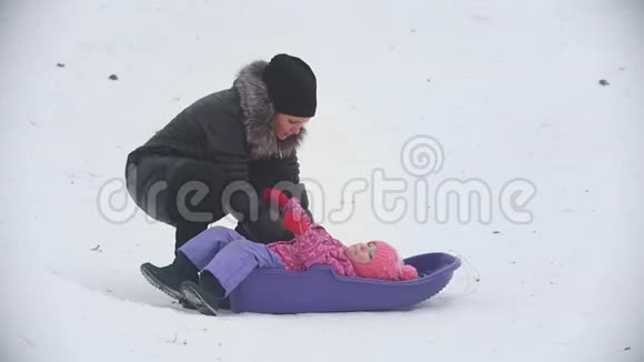 妈妈让他不听话的女儿坐在冬天的街道上雪橇上视频的预览图
