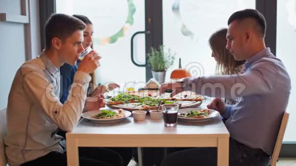 四个年轻的朋友在餐厅里和大比萨一起吃饭视频的预览图
