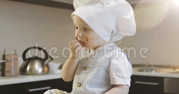 一个戴着烹饪帽的脏孩子在厨房里吃巧克力视频的预览图