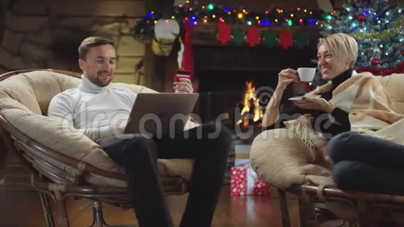 男人在网上购物时使用笔记本电脑和信用卡而女人则在圣诞节晚上喝咖啡视频的预览图