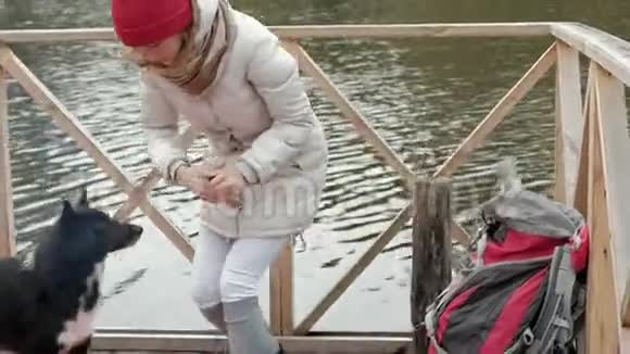 一位女游客坐在河岸附近的桥上喂狗做饭野餐积极休息健康视频的预览图