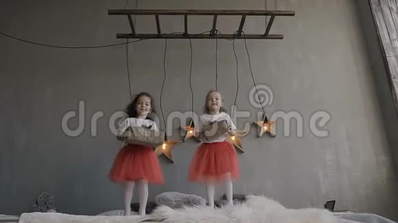 两个穿着红色裙子和一件白色T恤衫的小妹妹在床上蹦蹦跳跳地享受着他们收到的礼物视频的预览图