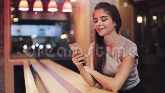 年轻女子坐在酒吧里用她的智能手机旁边的霓虹灯酒吧标志在交流中享受夜生活的女人视频的预览图