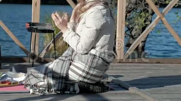 一位穿着保暖衣服的女游客在河岸附近的一座桥上背着背包喝着热茶野餐一只狗躺着视频的预览图