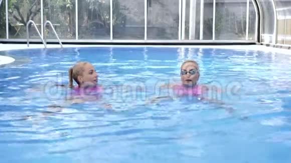 两个穿着粉红色泳衣的双胞胎金发女郎在蓝色的水池里游泳视频的预览图