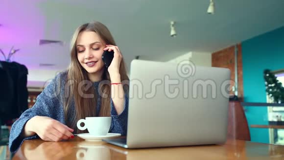 快乐的年轻时髦女人喝杯咖啡在咖啡馆里打电话桌上的笔记本电脑视频的预览图