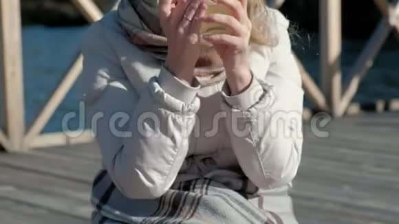 一位穿着暖和的衣服的女游客背着背包在河岸边的桥上喝着热茶野餐躺着一只狗视频的预览图