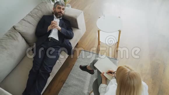 躺在沙发上谈论自己与专业女性心理治疗师或心理学家的问题的人的最高看法视频的预览图