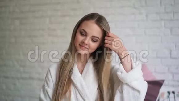 坐在床上的漂亮女孩扭着卷发美丽健康的头发视频的预览图