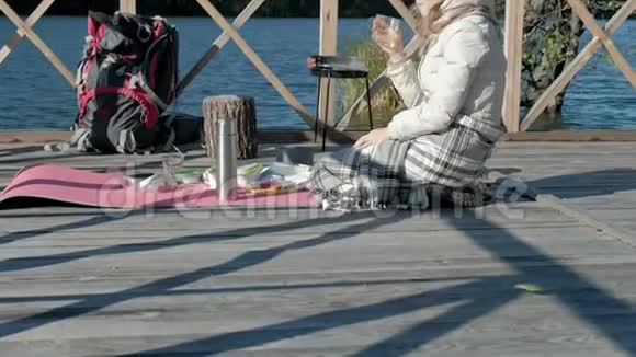 女游客穿着温暖的衣服在河岸边的桥上背着背包喝着热茶野餐积极休息视频的预览图