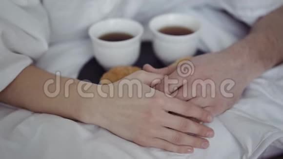 早餐咖啡和新鲜牛角面包在桌子上幸福的夫妇躲在毯子下牵手早上好视频的预览图