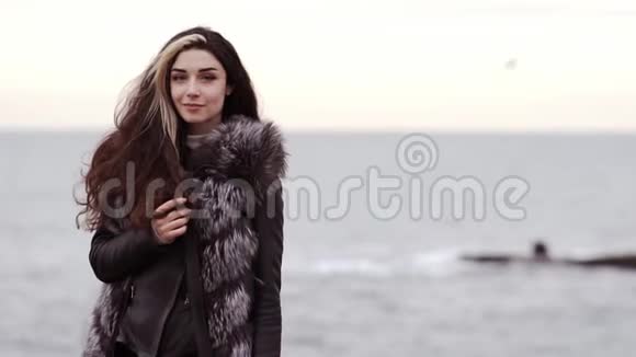 一位身穿毛皮外套的年轻黑发女子的肖像她在冬天站在海边海浪拍打地面引起了人们的注意视频的预览图