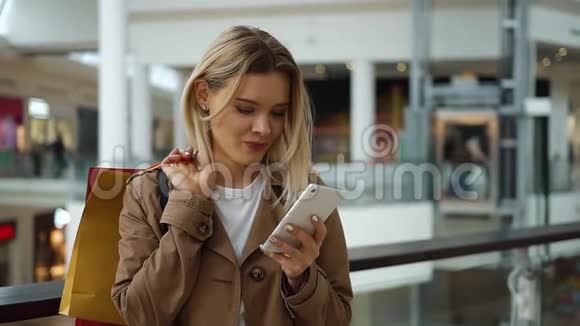 女孩检查她的手机站在她的肩膀上的购物袋在商场视频的预览图
