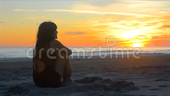 性感的女人看着海滩上美丽的日落愉快地微笑着视频的预览图