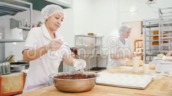 女面包师把巧克力奶油混合在金属碗里做蛋糕视频的预览图