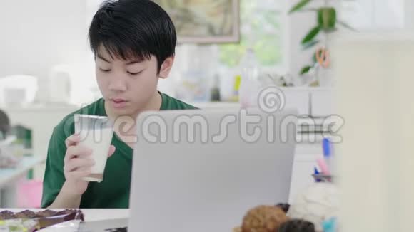 亚洲小男孩在智能手机上使用卷轴同时慢慢地吃有机牛奶早餐视频的预览图