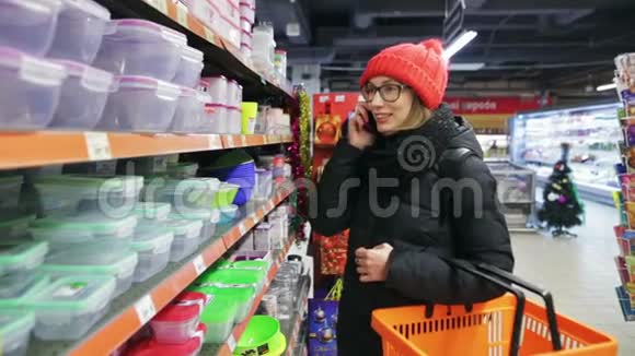 一个年轻的现代女孩正在超市购物用手机聊天真诚的微笑她选择了塑料视频的预览图