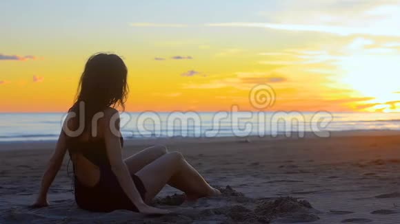 性感年轻的黑发女人在日落时躺在沙滩上玩视频的预览图