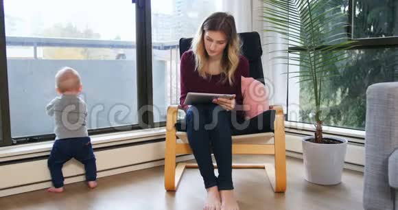 母亲在照顾婴儿时使用数码平板电脑视频的预览图