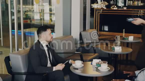 一位性格开朗的白人商人和他的搭档坐在一起用他的智能手机在网上付账视频的预览图