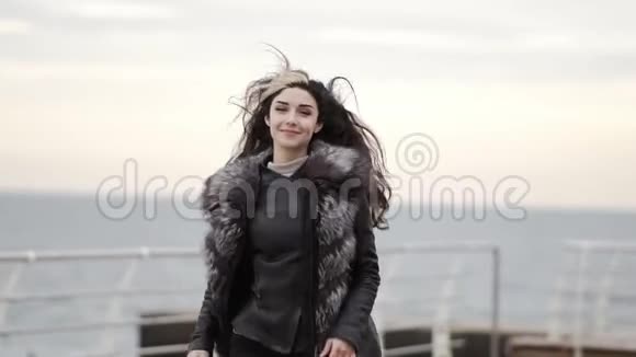 一个年轻的黑发女人的肖像穿着毛皮外套在冬天在大海或海洋边奔跑转过身来微笑着她是视频的预览图