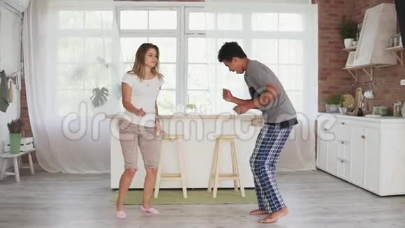 快乐的多民族夫妇穿着睡衣在厨房跳舞有魅力的一对相爱的夫妇在家玩得很开心慢动作视频的预览图