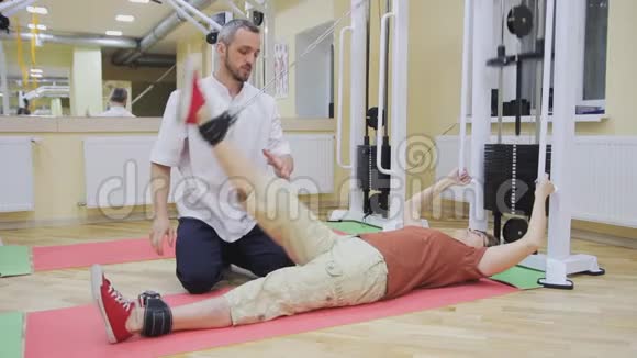 理疗师帮助老年妇女抬腿在健身房做运动健康体操活跃的人视频的预览图