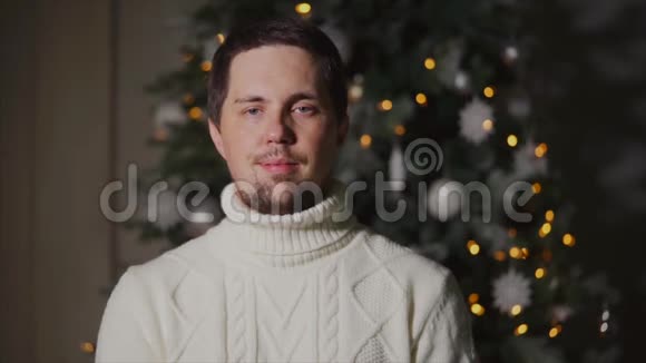 站在圣诞树前的一个穿着暖和毛衣的人的肖像视频的预览图