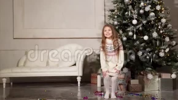 快乐的小女孩在假日的早晨在圣诞树附近的大厅里跳视频的预览图