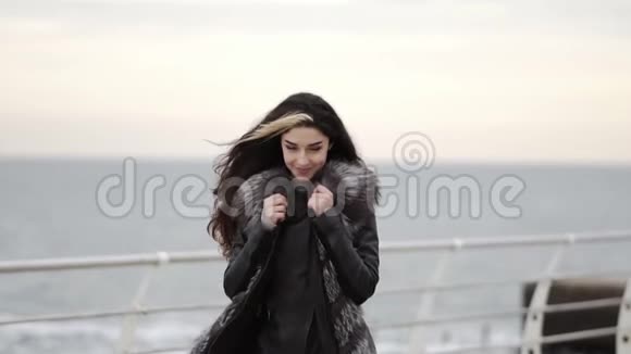 迷人的快乐黑发女人穿着毛皮外套站在海边冬天转过身来微笑着她在找视频的预览图