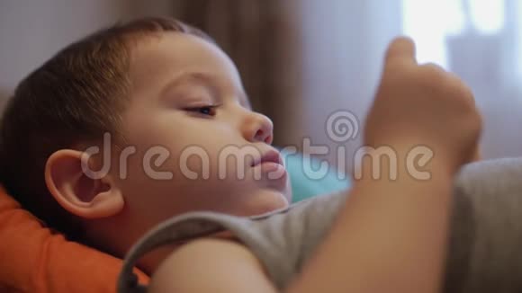 CU开心的脸上的孩子一个小男孩躺在沙发上的手机快乐的童年视频的预览图