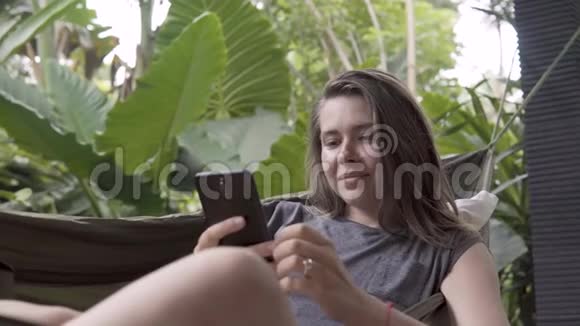 女人坐在吊床上在智能手机上写留言自然背景视频的预览图