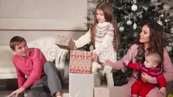 幸福友好的家庭在大圣诞树下折叠礼物视频的预览图