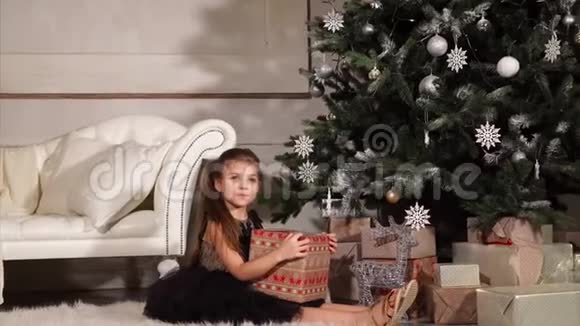 在庆祝活动的晚上漂亮的小女孩正坐在圣诞树下视频的预览图