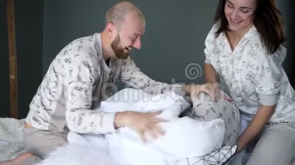 一家人抱着枕头在床上胡闹父母带着一个穿着相同睡衣的孩子在卧室里视频的预览图