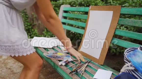 女孩艺术家准备纸调色板和油漆刷在公园的风景画与一个小池塘4k视频的预览图