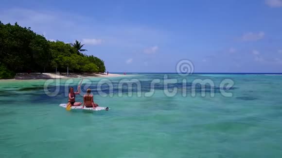 两个漂亮的年轻女孩坐在冲浪板上在温暖的蓝色海水中鸟瞰视频的预览图