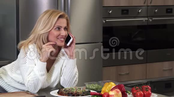 在厨房打电话的快乐成熟的女人视频的预览图